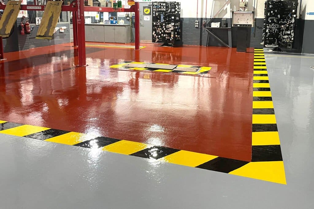 Finished garage workshop floor, showing yellow and black hazard strips around raised metal grill area