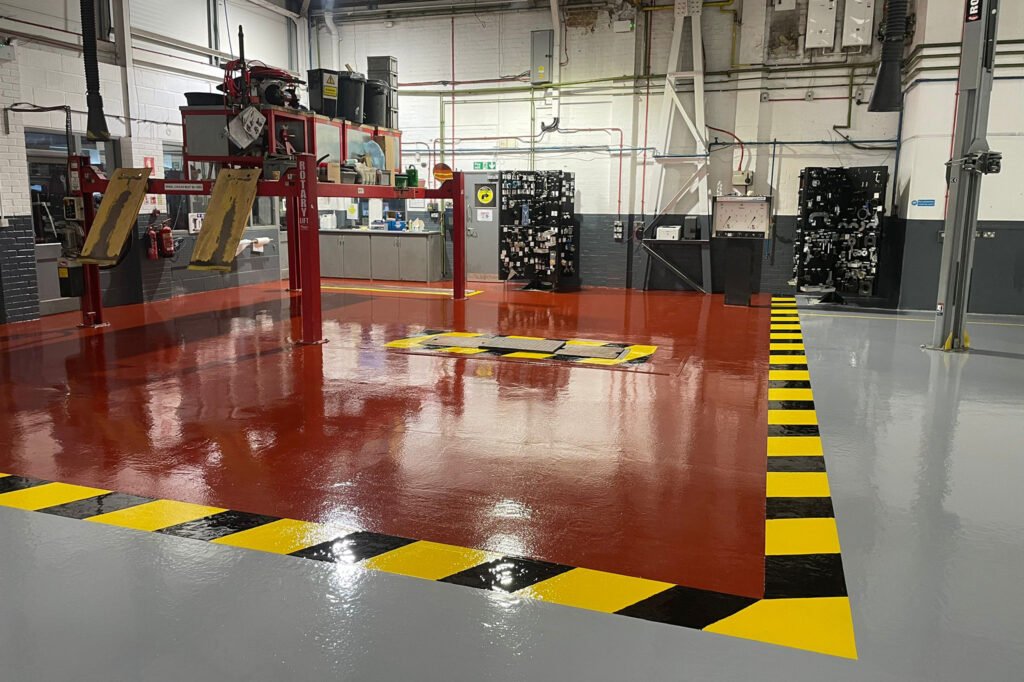 Resurface 1000㎡ garage floor, wellingborough with lfs high build ( a 2 component coloured epoxy resin floor coating Wide shot of finished garage workshop floor, showing yellow and black hazard strips separating grey and red epoxy coatings