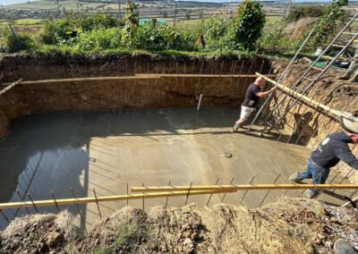 Contractors working with concrete inside the newly dug hole for a swimming pool