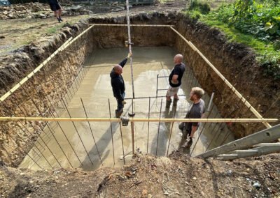 Contractors working with concrete inside the newly dug hole for a swimming pool