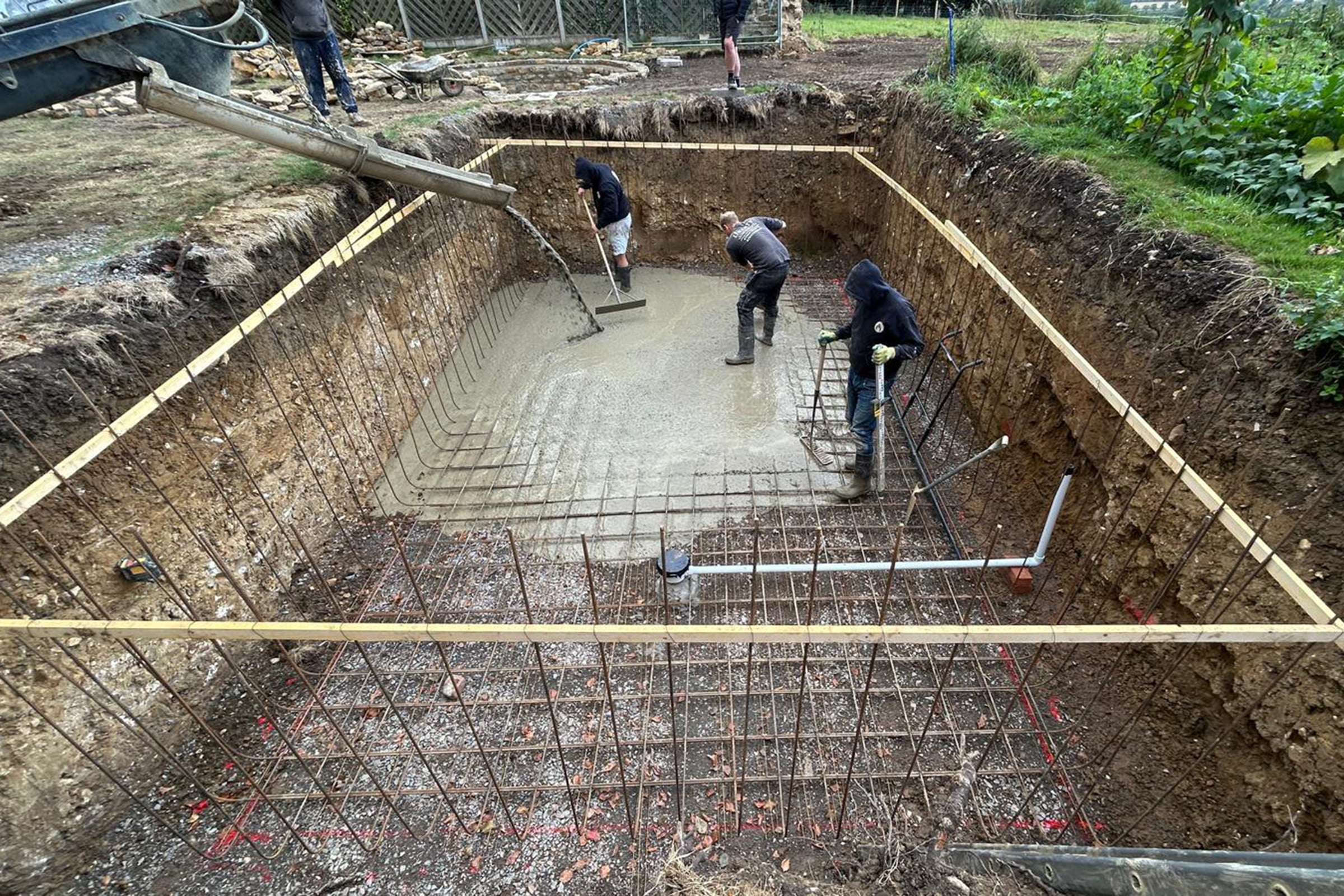 Contractors pouring concrete onto rebar grid in a newly dug hole for a swimming pool