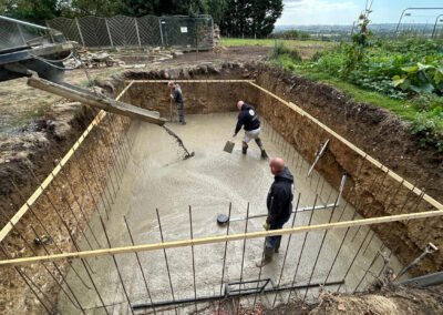 Contractors pouring concrete into the newly dug hole for a swimming pool
