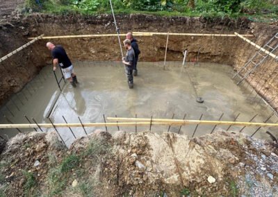 Contractors tamping down concrete inside the newly dug hole for a swimming pool