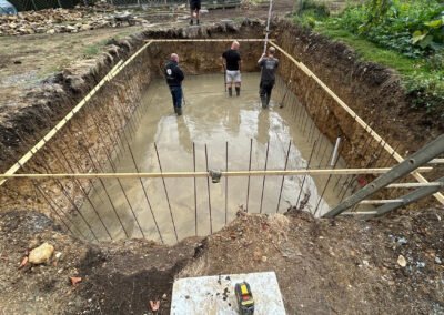 Contractors tamping down concrete inside the newly dug hole for a swimming pool
